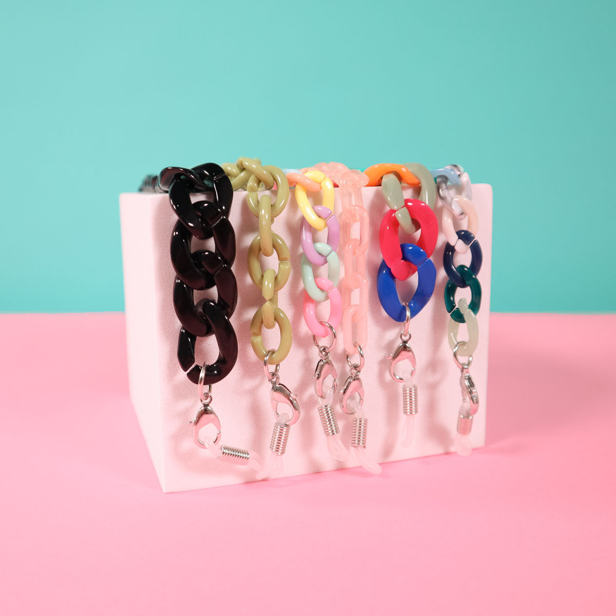 Multi coloured mask and glass chains on a blue pink background.