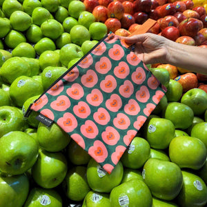 Reusable floral-patterned bag held over a pile of green apples in a grocery store.