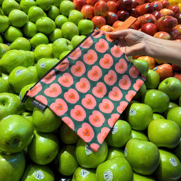 Reusable floral-patterned bag held over a pile of green apples in a grocery store.