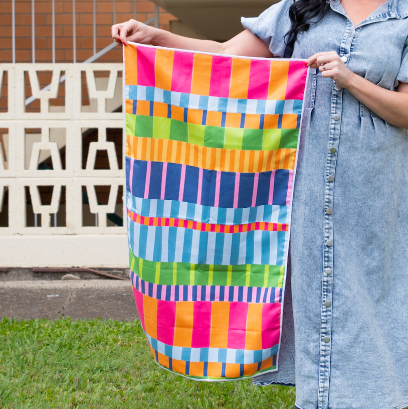 A person holding a small towel with a vibrant striped pattern in multiple colors, including pink, green, orange, and blue.