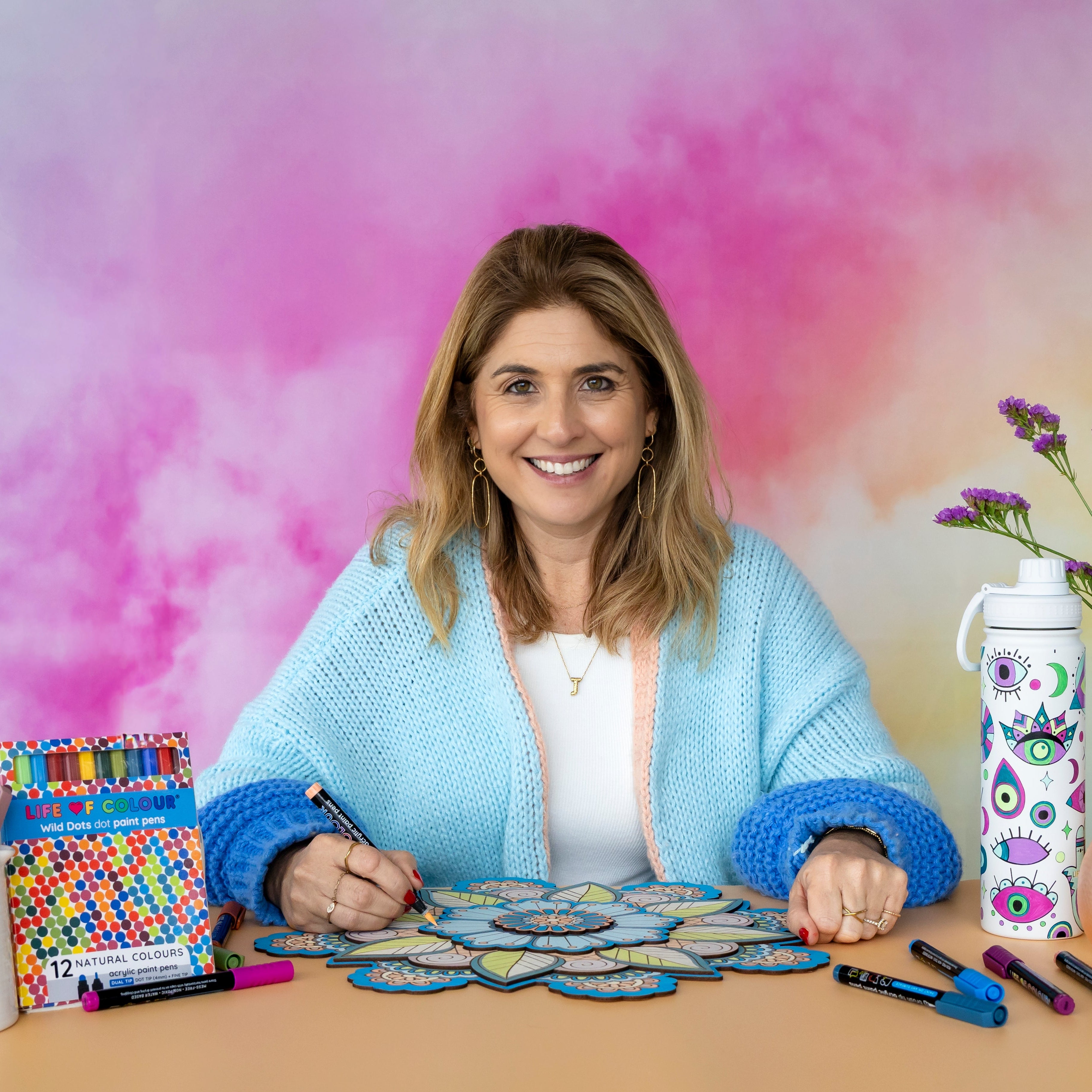 Woman sitting at a table with art supplies and a colorful background