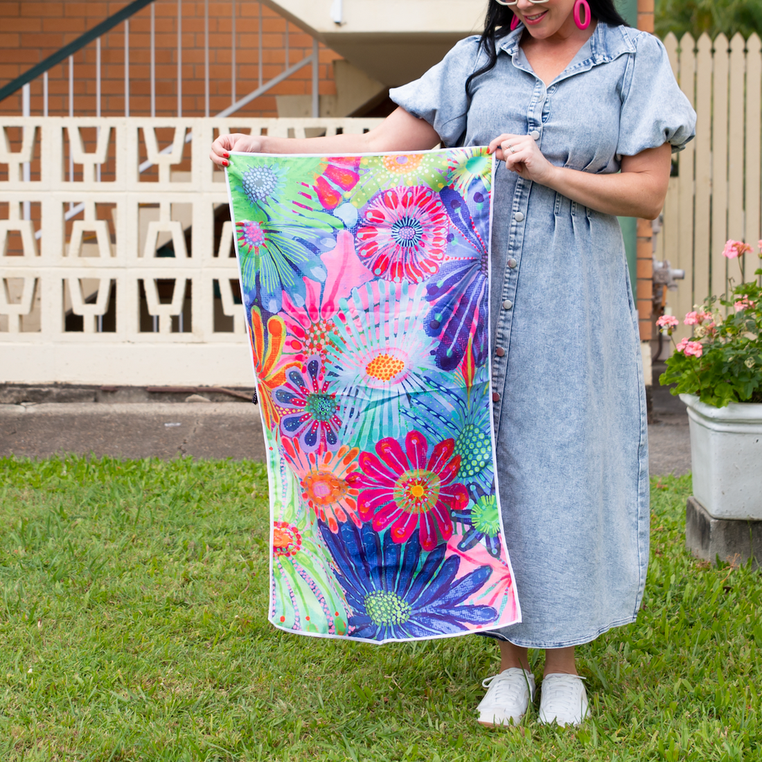A person holding a small towel with a vibrant floral design in a garden setting.