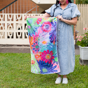 A person holding a small towel with a vibrant floral design in a garden setting.