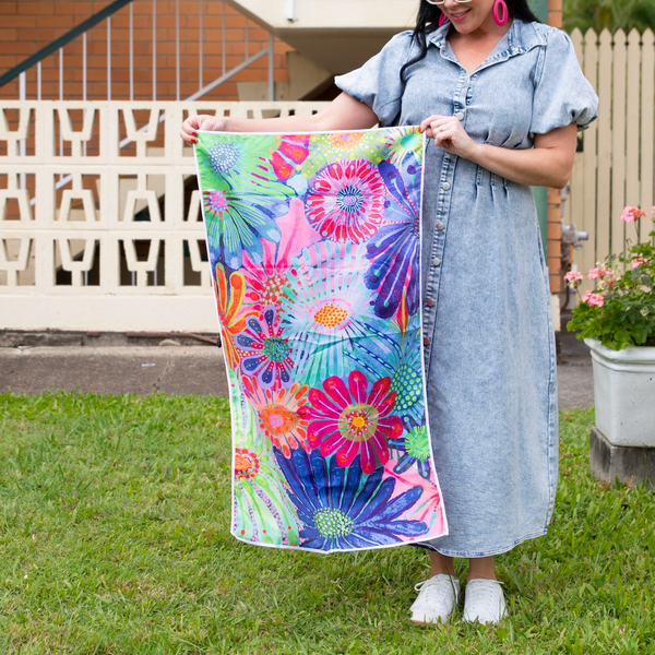 A person holding a small towel with a vibrant floral design in a garden setting.
