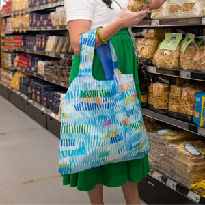 Person shopping in a grocery store aisle with a colorful reusable bag.