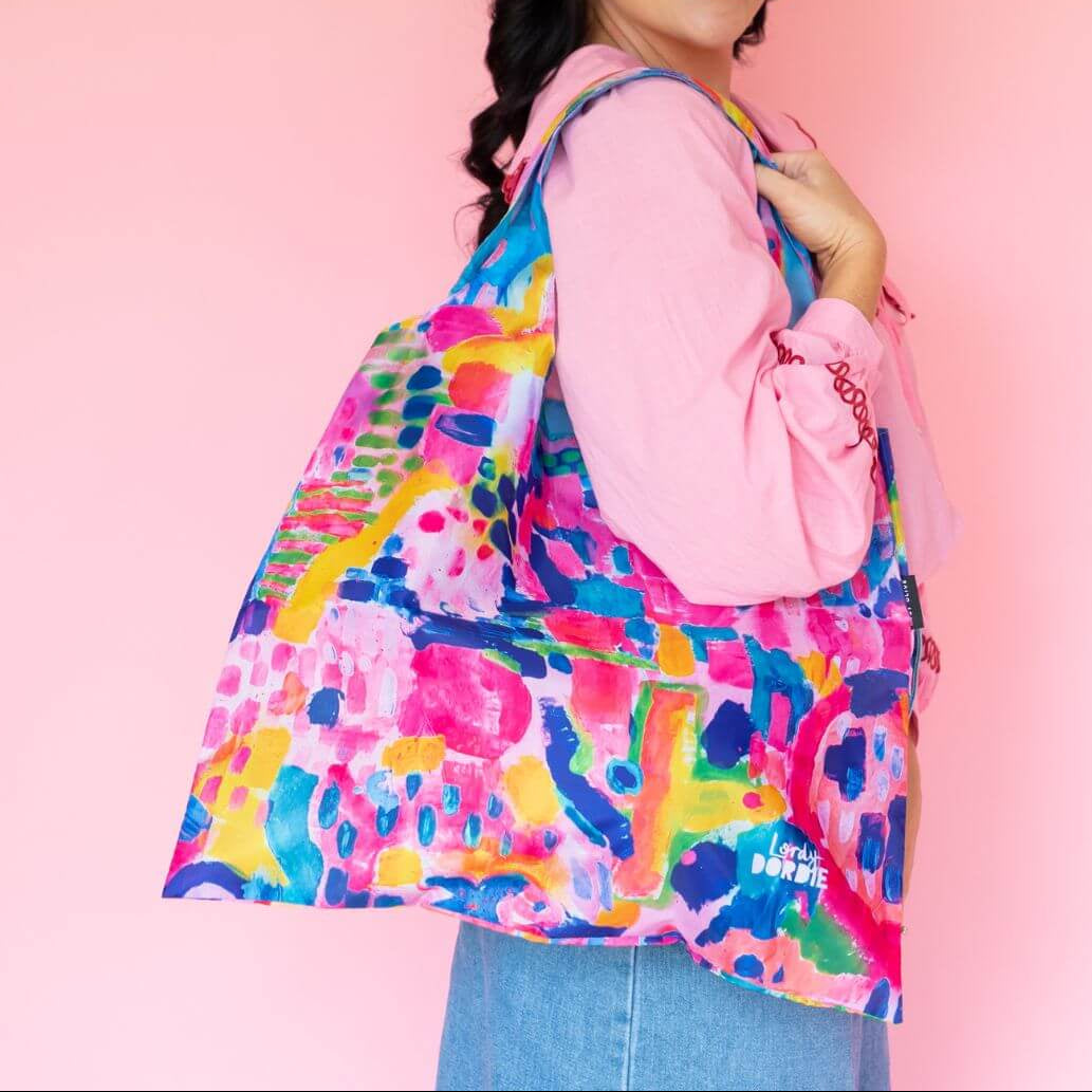 Woman holding a colorful patterned bag against a pink background