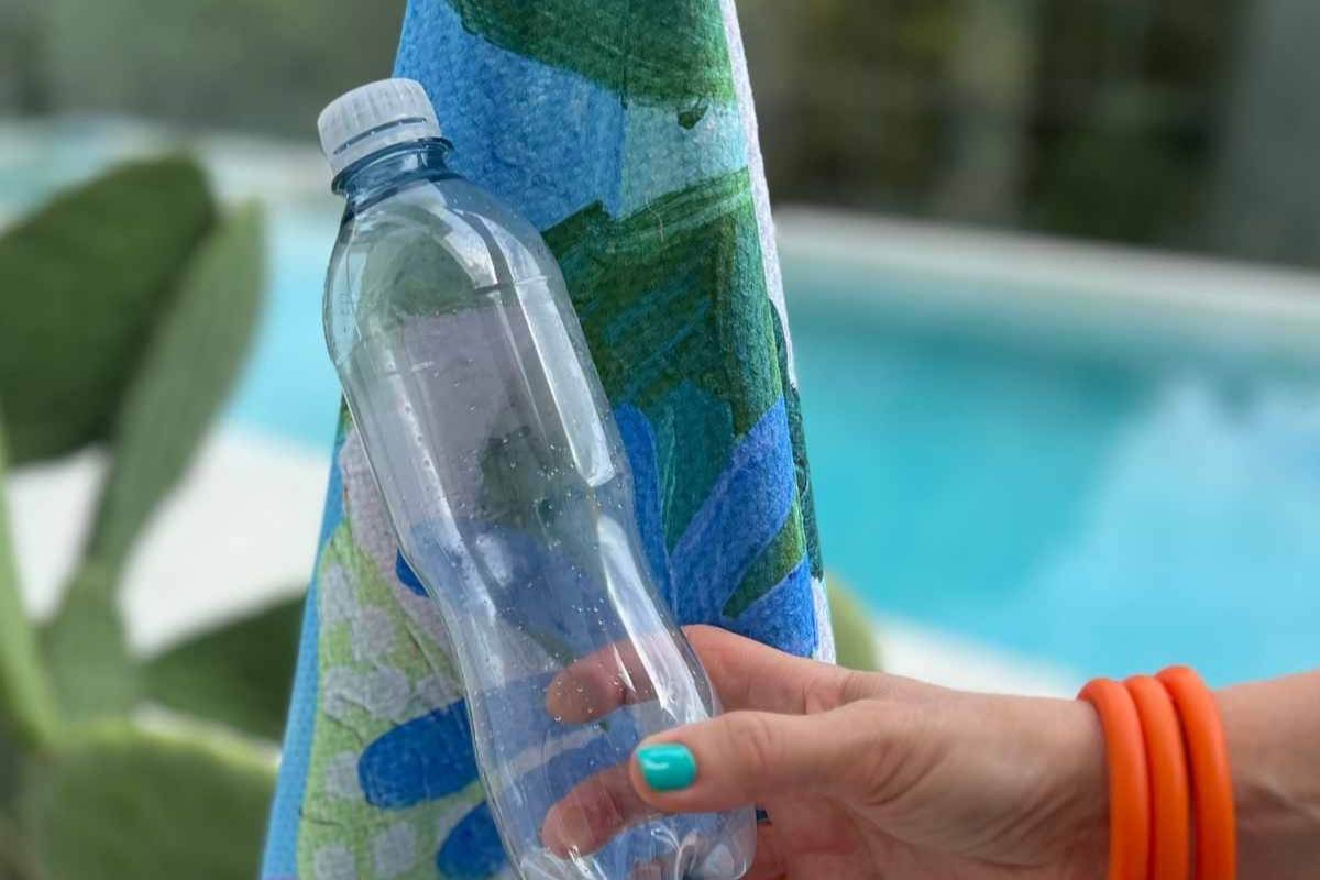 Hand holding a clear water bottle with a blue towel in the background