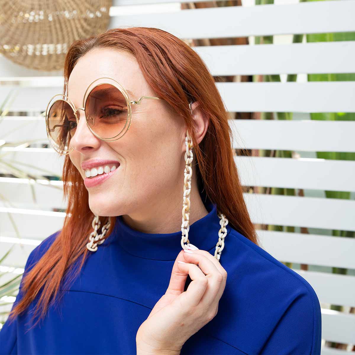 Smiling women wearing sunglasses with a beige chain. 