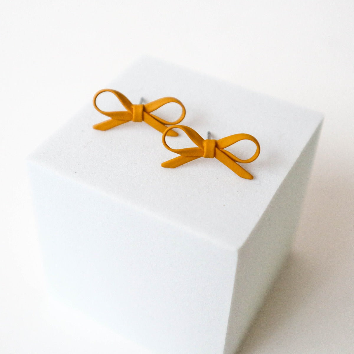 Mustard yellow bow shaped stud earrings on a white background.