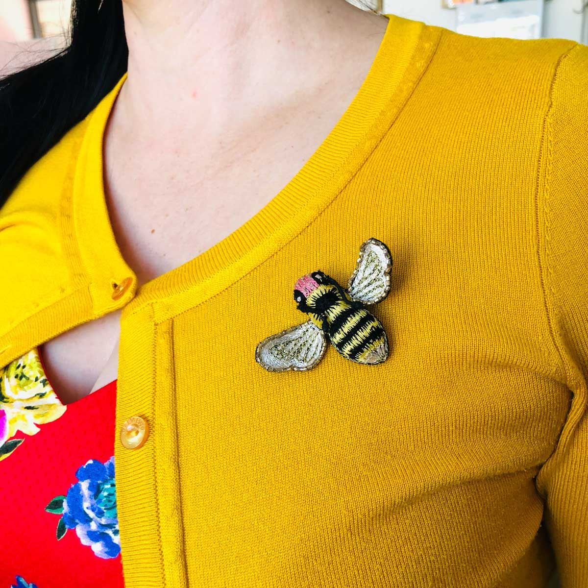 Embroidered bumblebee brooch on a mustard yellow cardigan. 