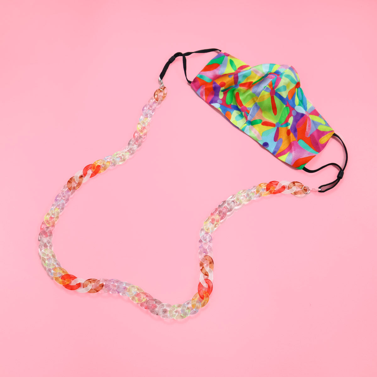 Flat lay of bright neon face mask and candy coloured glasses chain. 