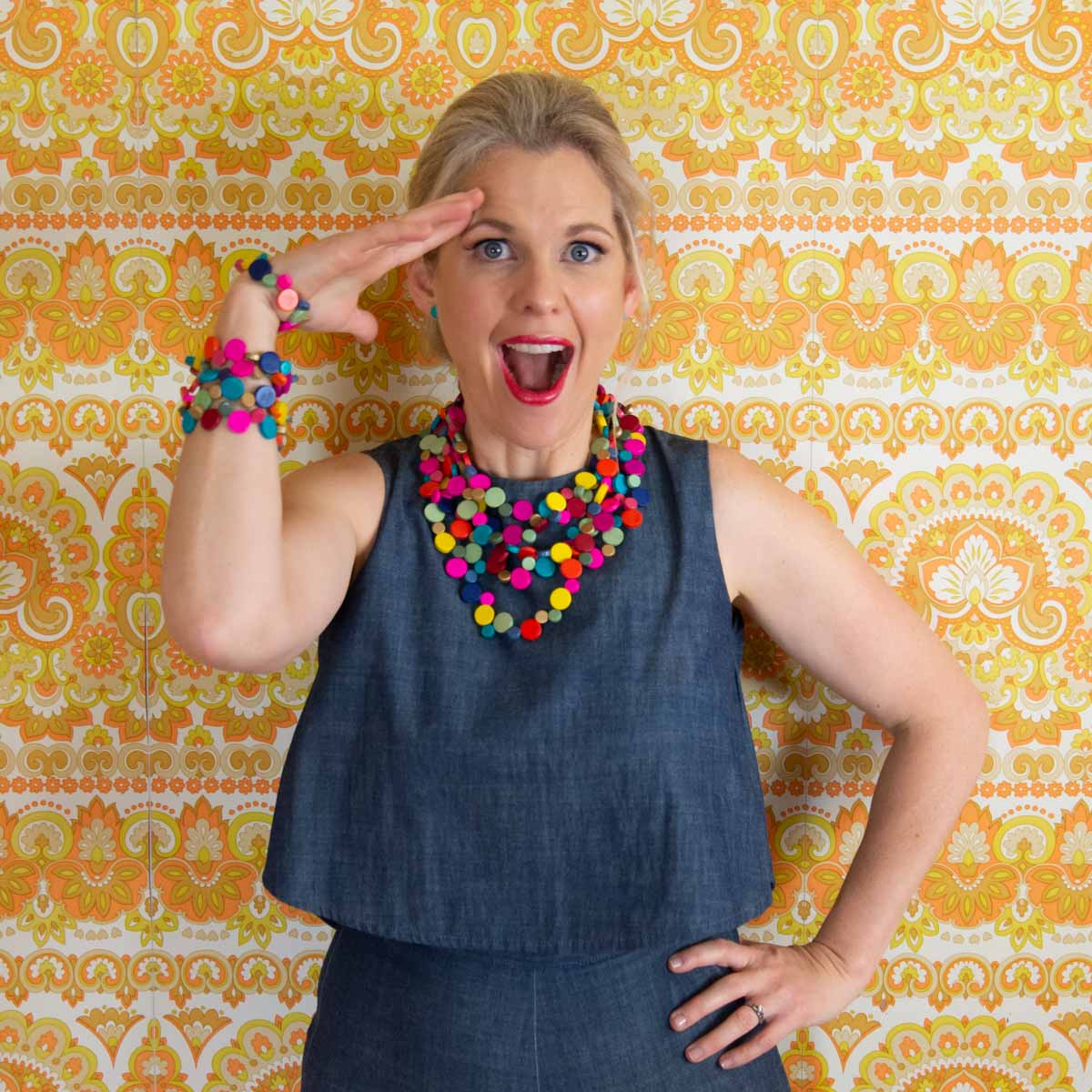 Women posing with rainbow coloured jewels in front of vintage orange and yellow background.