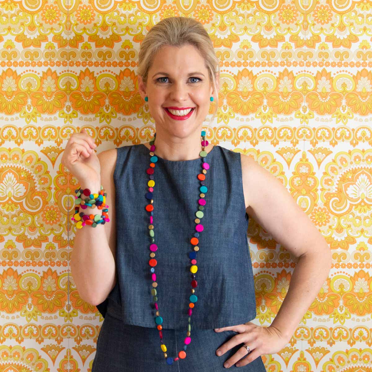 Women posing with rainbow coloured jewels in front of vintage orange and yellow background.