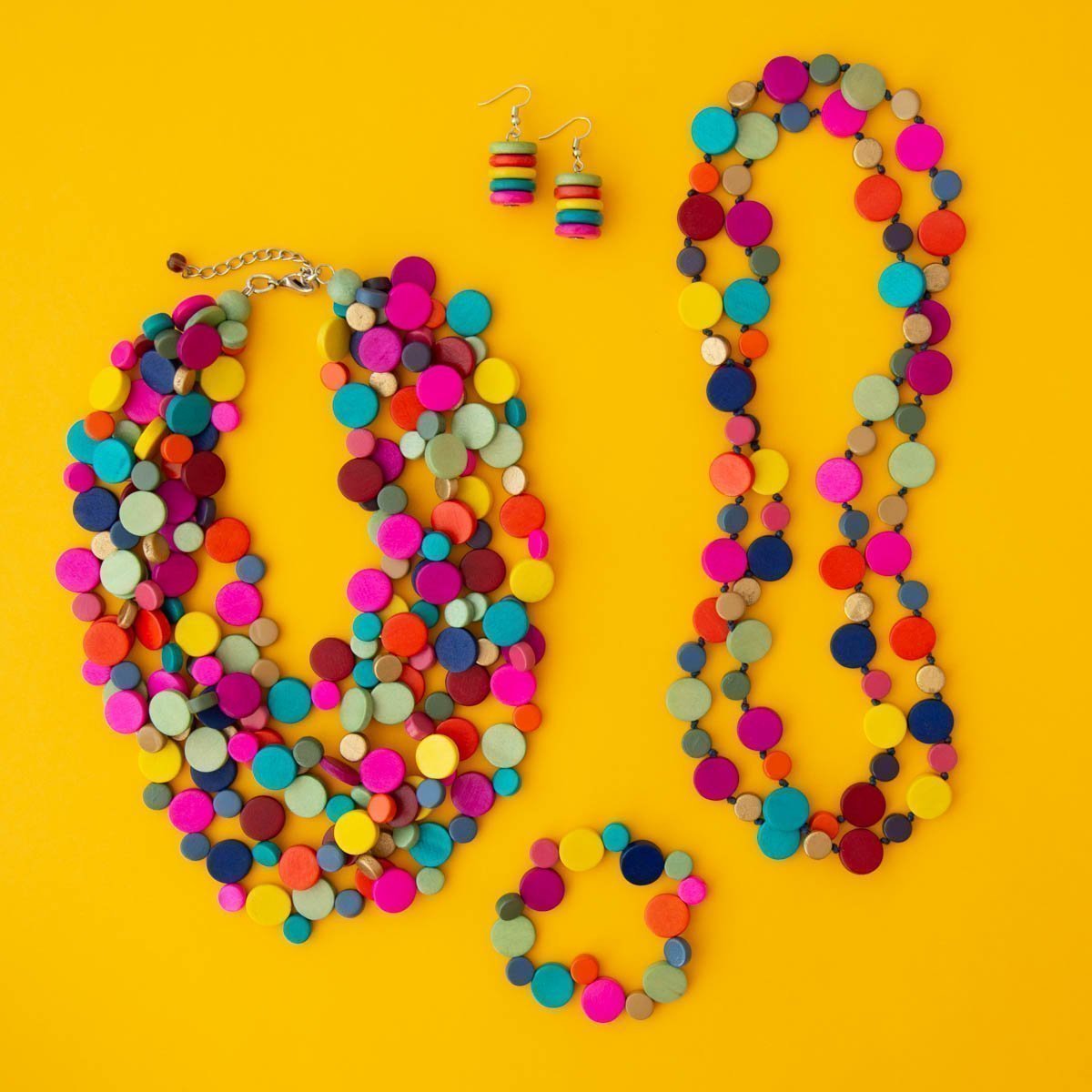 Rainbow coloured jewellery collection featuring necklace, bracelet and earring on a yellow background.