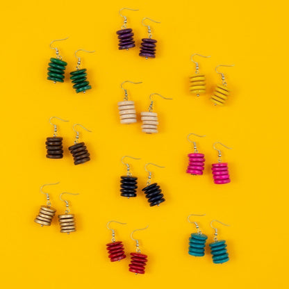 Multiple bright stacked wood drop earrings on yellow background.
