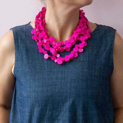 Close up of women wearing a denim jumpsuit and a bright hot pink wood stacked necklace.