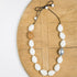 White wood pod shaped necklace on a light wood background.